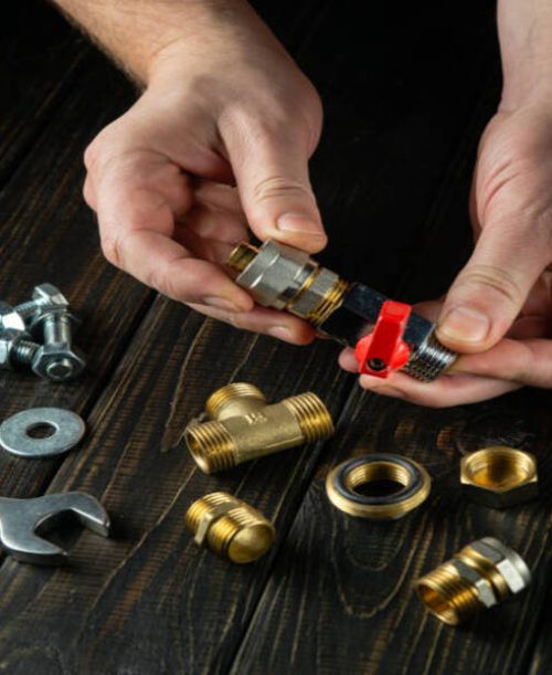 A plumber connects brass fittings to a water tap. Close-up of a master hand while working in a workshop